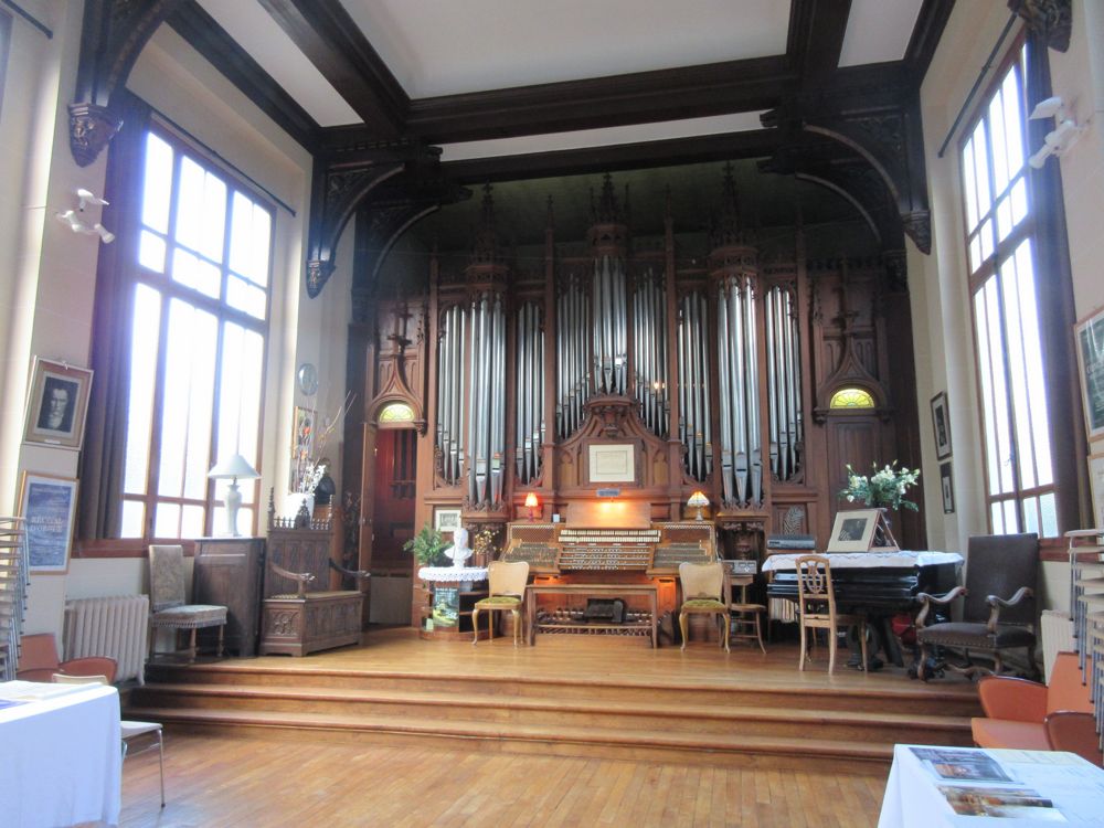 organ console and facade with a piano and chairs beside