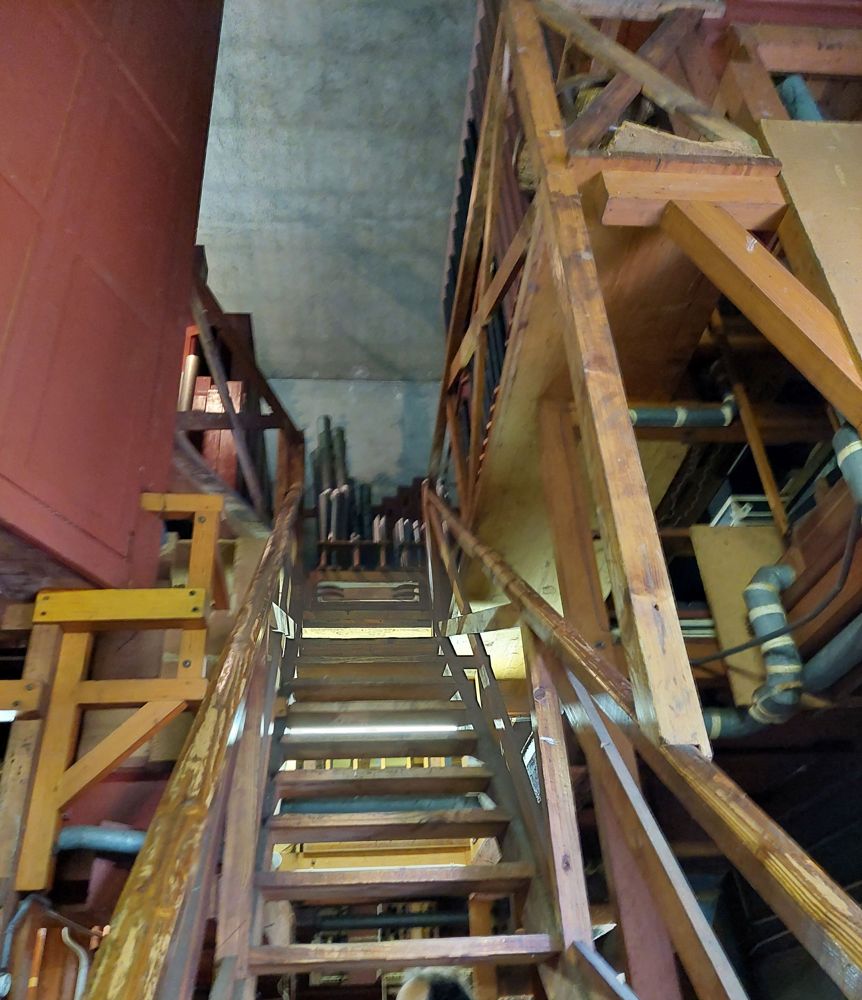 wooden stairs leading to pipes straight ahead. To the left and right are ducts and wooden structure holding more pipes.