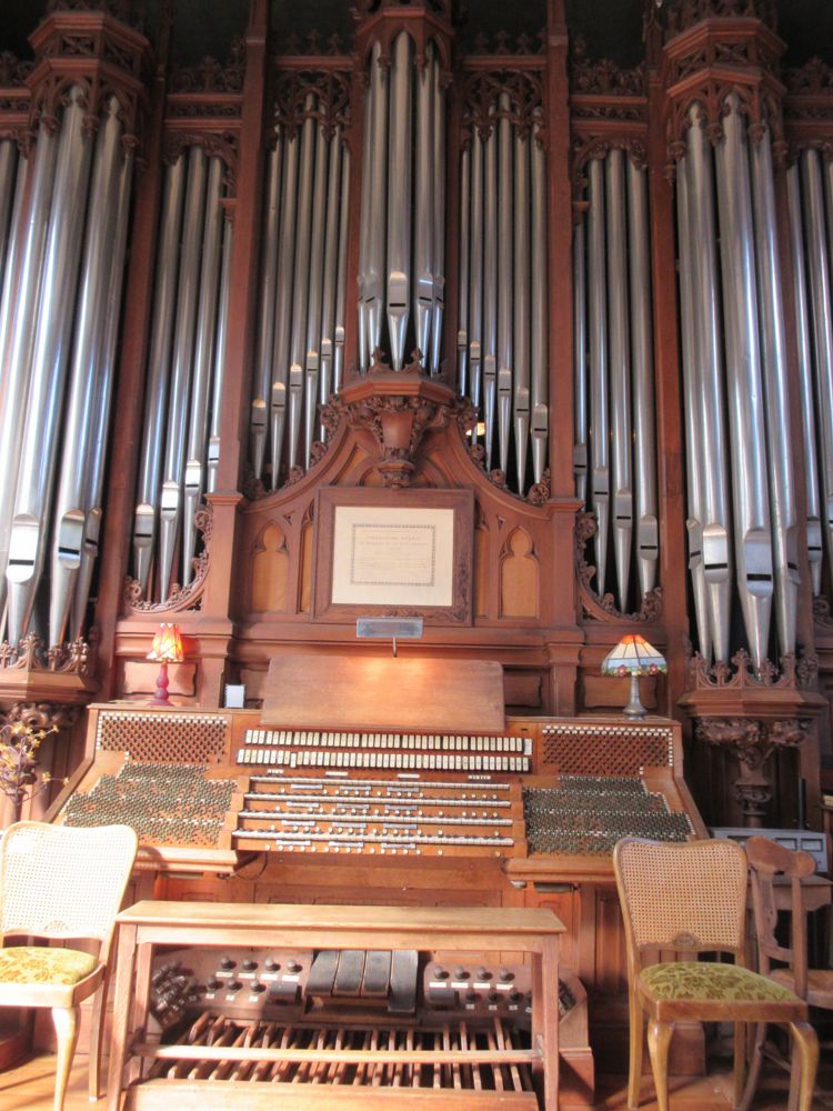 organ console with facade pipes above. There are four manual and two rows of stops above them. To the left and right are a lot of other switches.